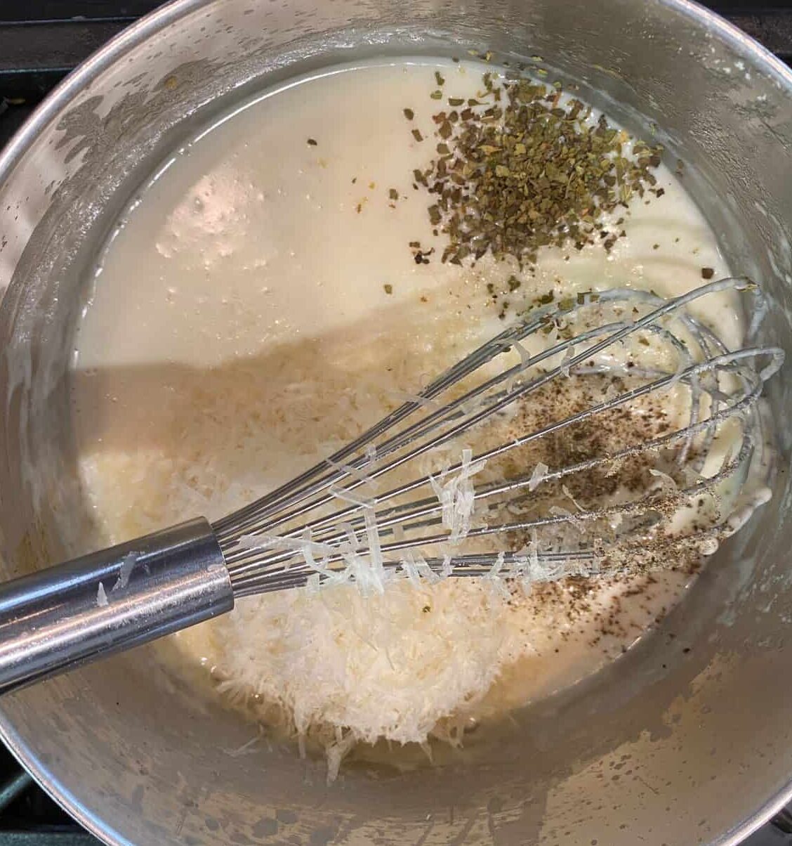 White sauce with parmesan and oregano and a whisk.