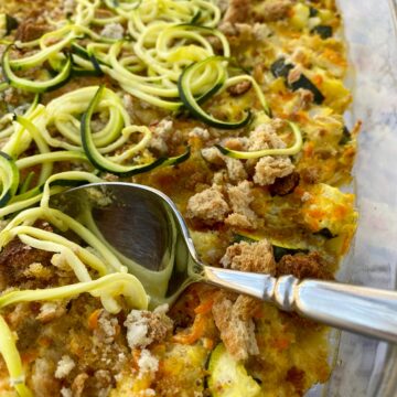 Baking dish with zucchini casserole and a serving spoon.