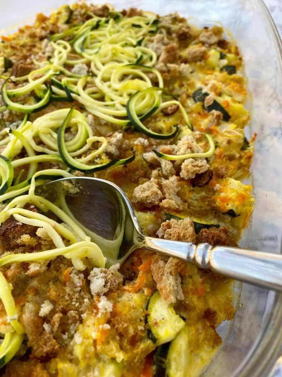 Baking dish with zucchini casserole and a serving spoon.