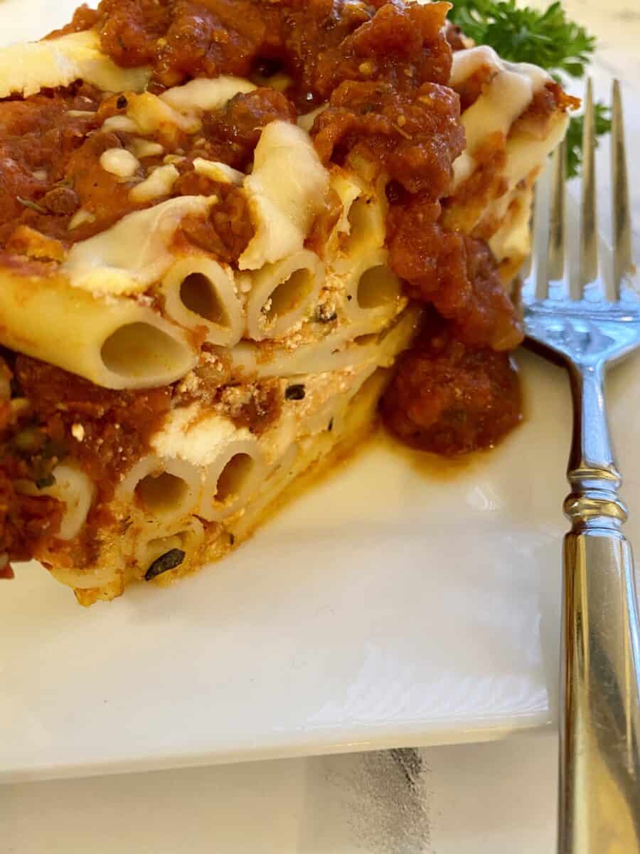 Baked ziti on a plate with sauce on the top and a fork on the side.