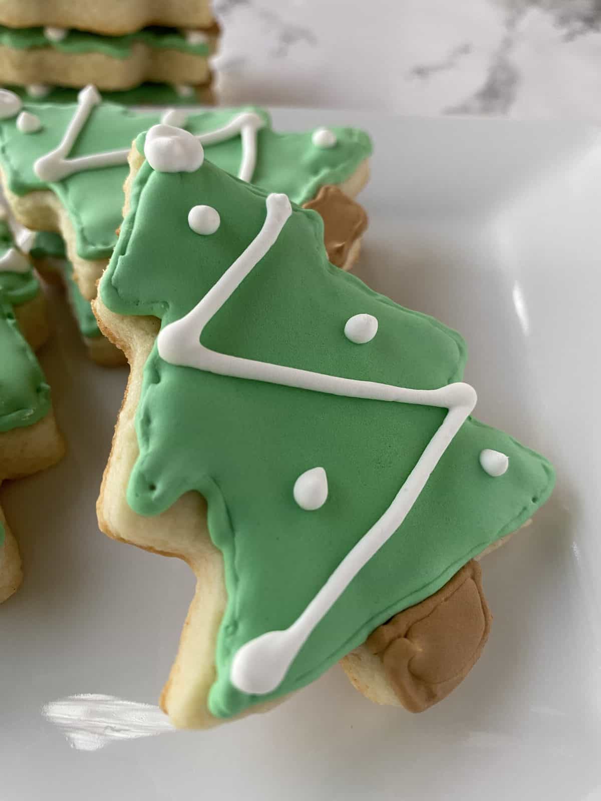 Sugar cookies shaped like Christmas trees on a plate.