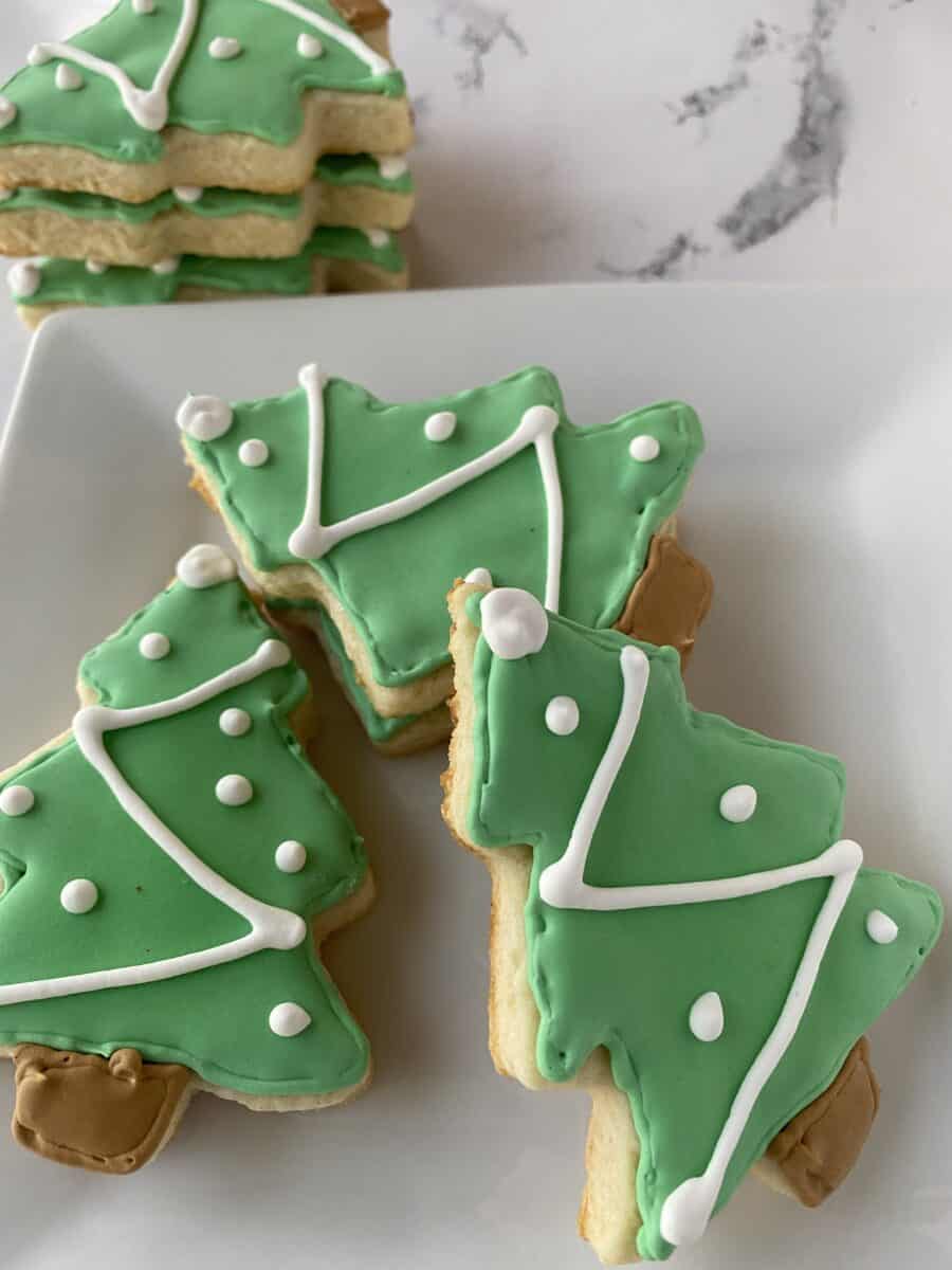 Sugar cookies shaped like Christmas trees stacked and arranged on a plate.