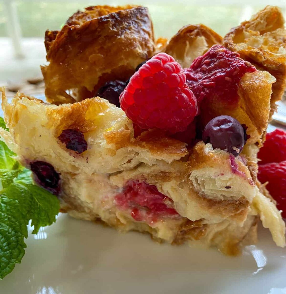 A portion of bread pudding on a plate with fresh raspberry on top.