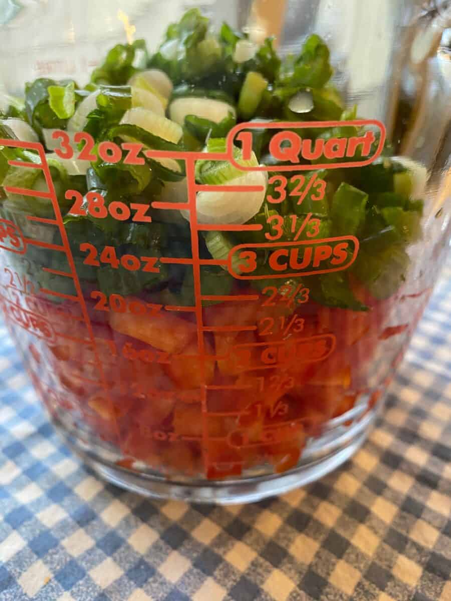 Diced red peppers and chopped green onions in a measuring cup.