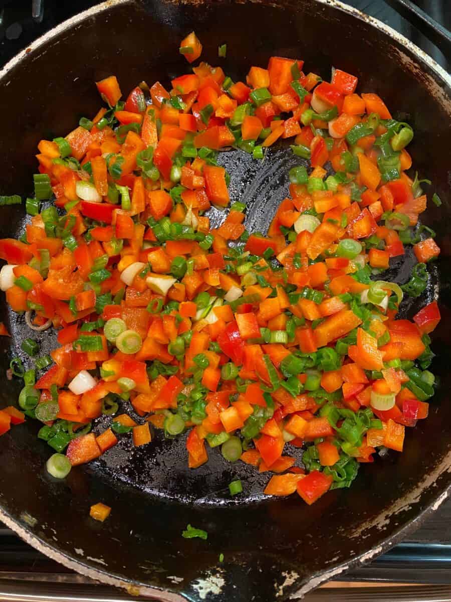 Diced red peppers and chopped green onions in a skillet on the stove.