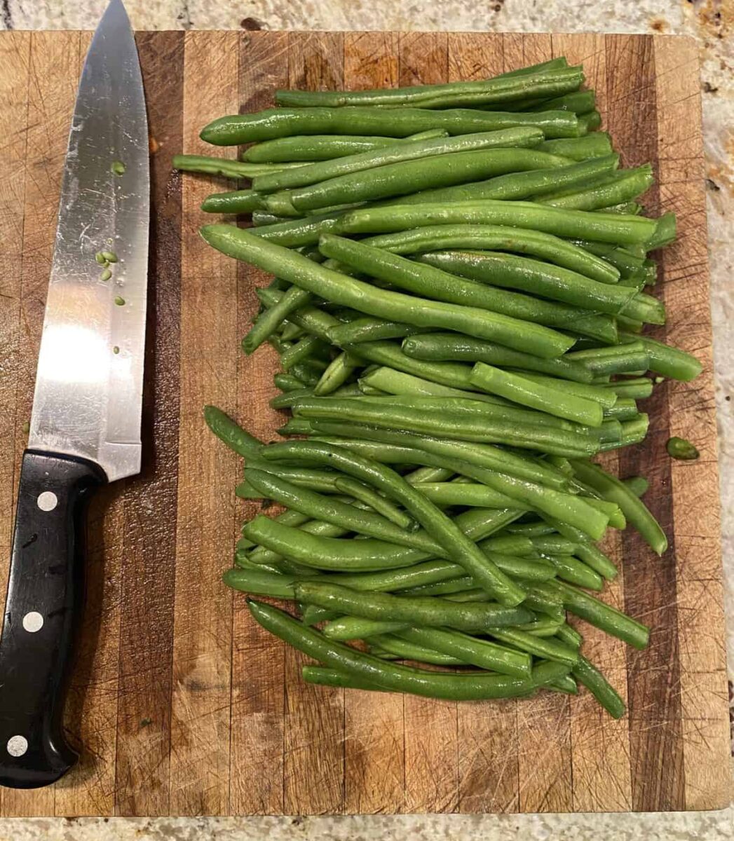 Green beans and a knife on a cutting board.