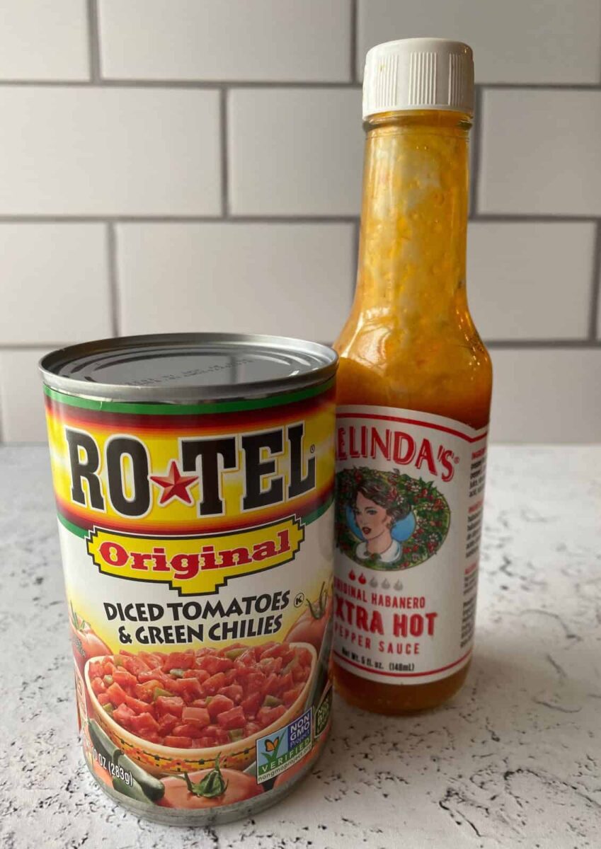 One can of tomatoes and a jar of hot sauce on a counter.