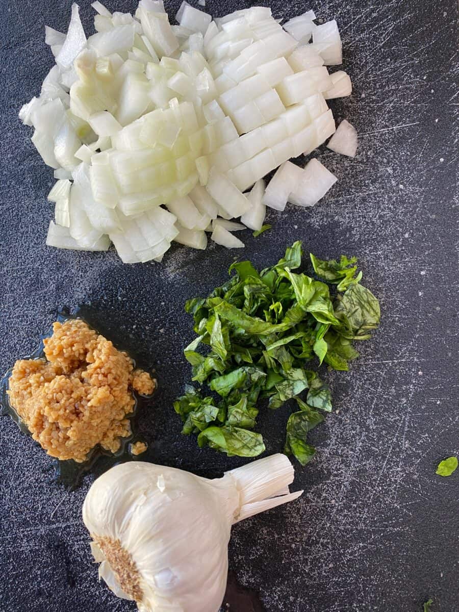 Chopped onion, garlic and basil on a cutting board. 