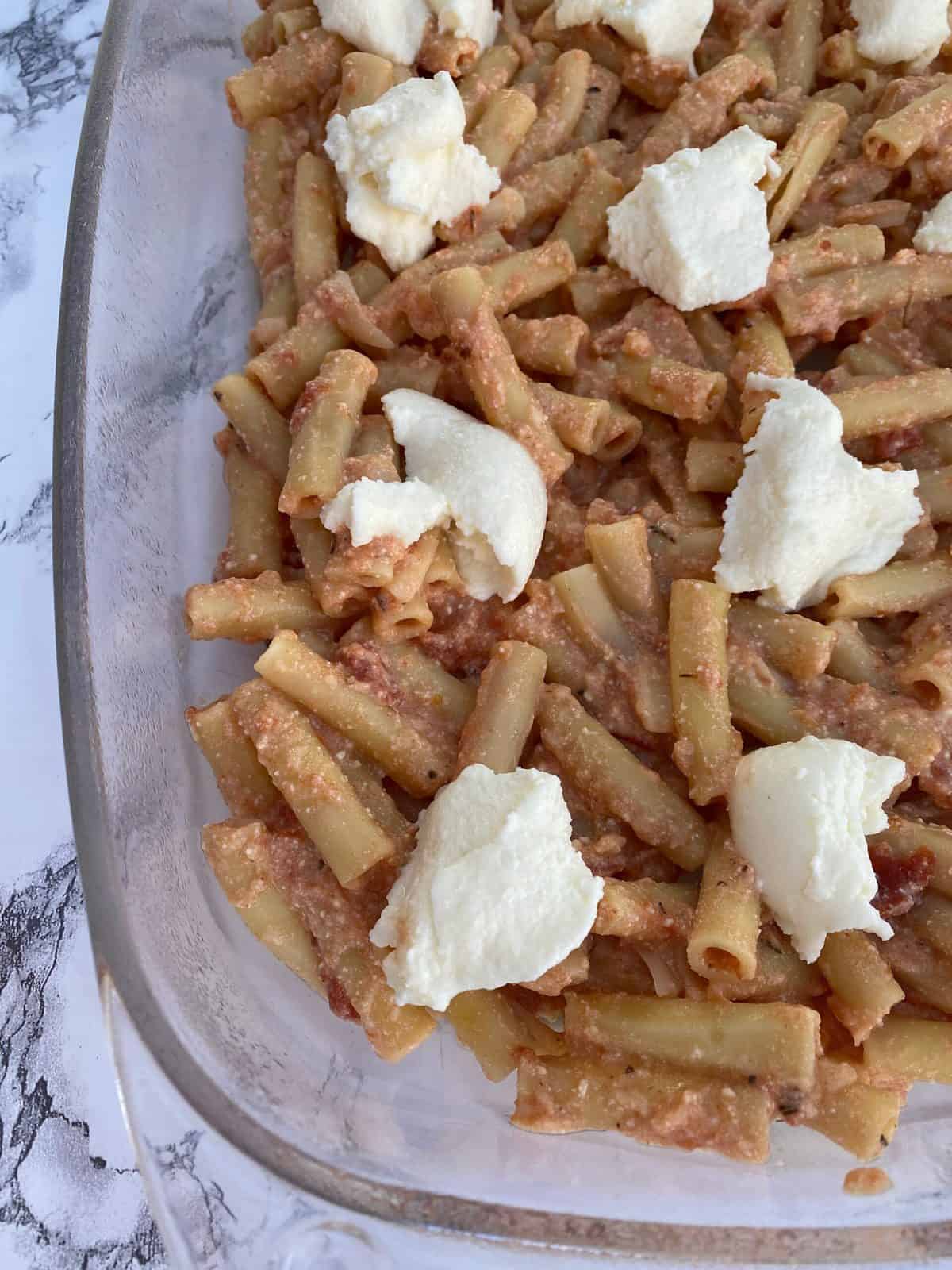Ziti pasta in a baking dish with cheese.