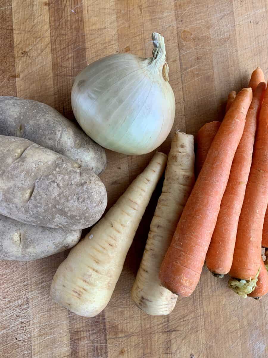 Potatoes, onion, parsnips and carrots on a cutting board. 