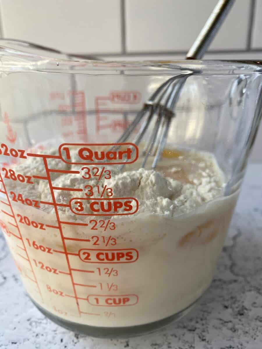 Milk, eggs and flour in a glass measuring cup with a whisk.