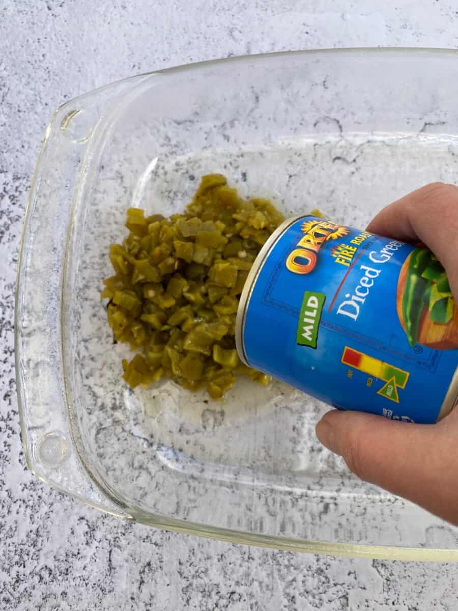 Canned green chilis being poured into a baking dish.