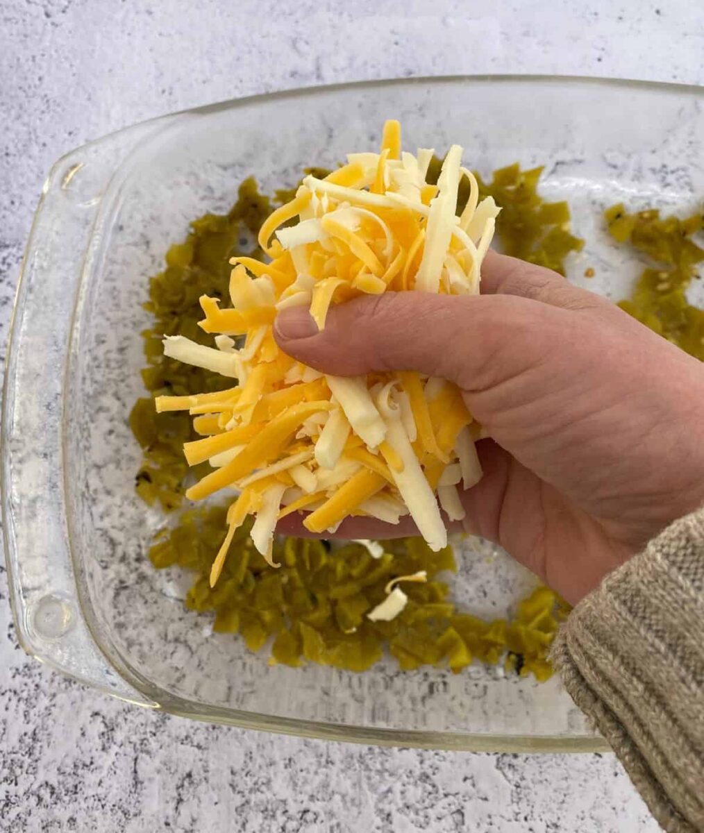 A handful of shredded cheese over a dish of green chilis.