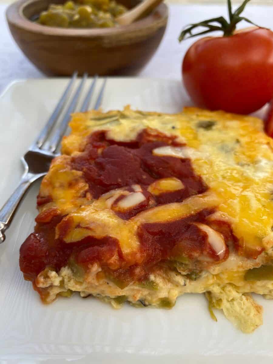 A serving of the chili relleno casserole with tomatoes and a small bowl of salsa.