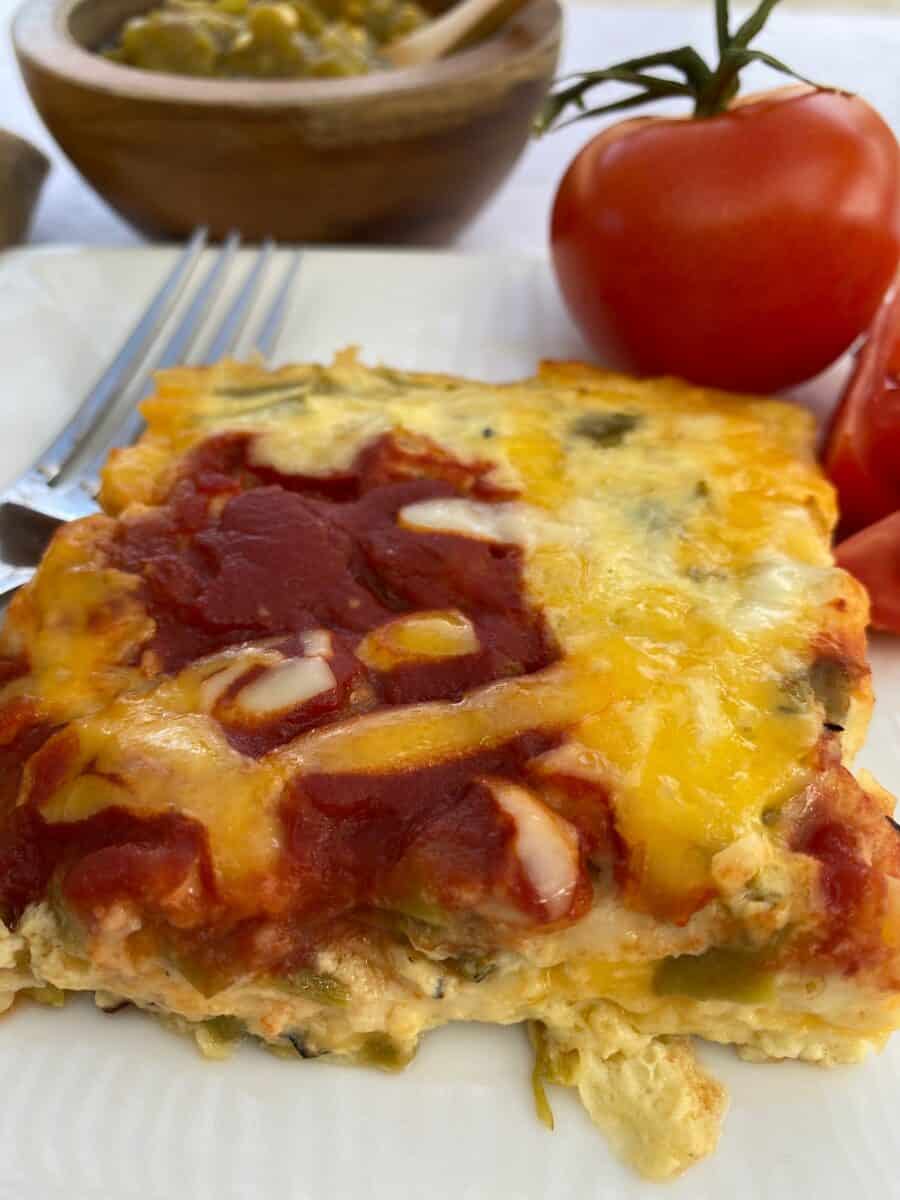 Side view of the casserole with tomatoes and a bowl of salsa in the background.