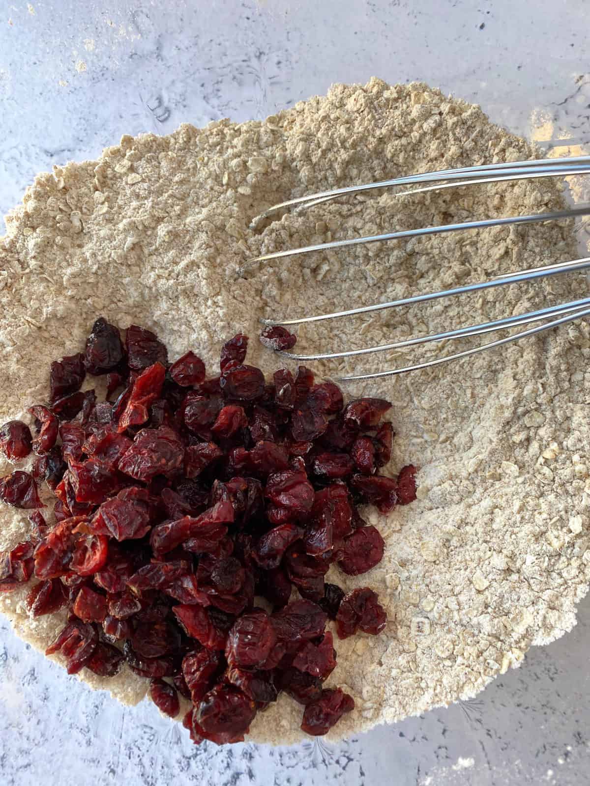 Dried cranberries and dry ingredients in a bowl with a whisk.