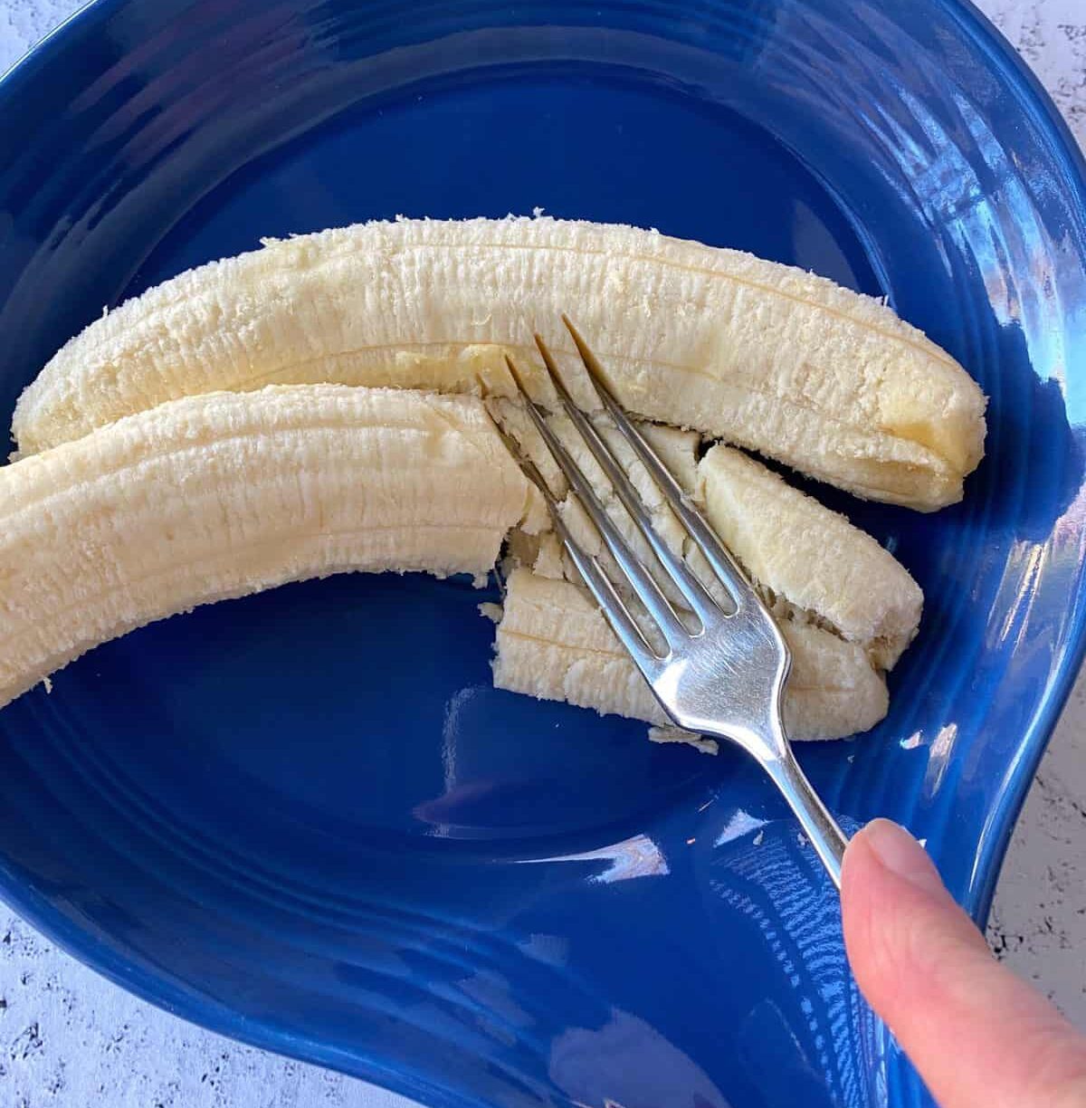 Two bananas in a dish, with a fork mashing them.