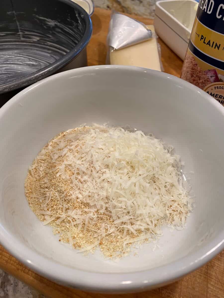 Dried bread crumbs and parmesan cheese in a small bowl on a cutting board.