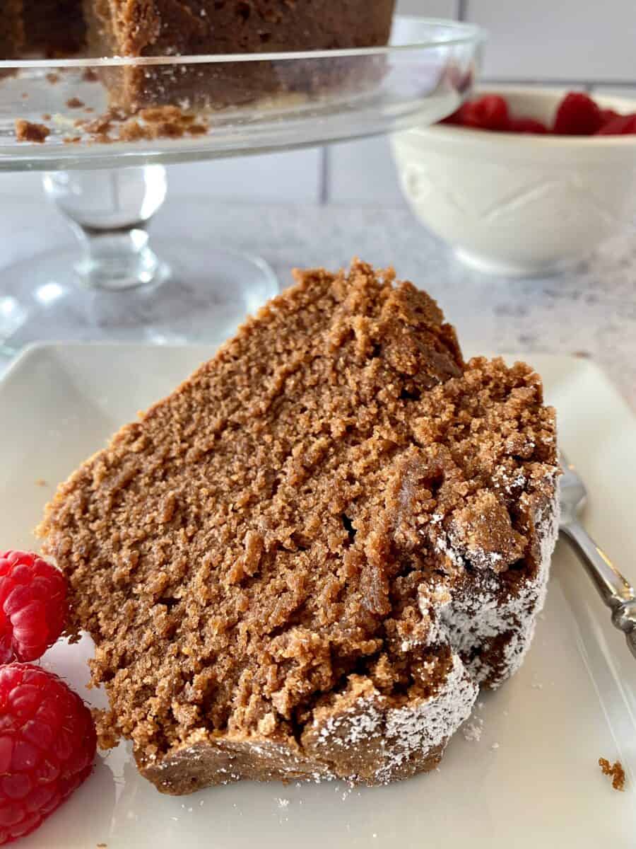 A slice of chocolate pound cake with raspberries on the side.