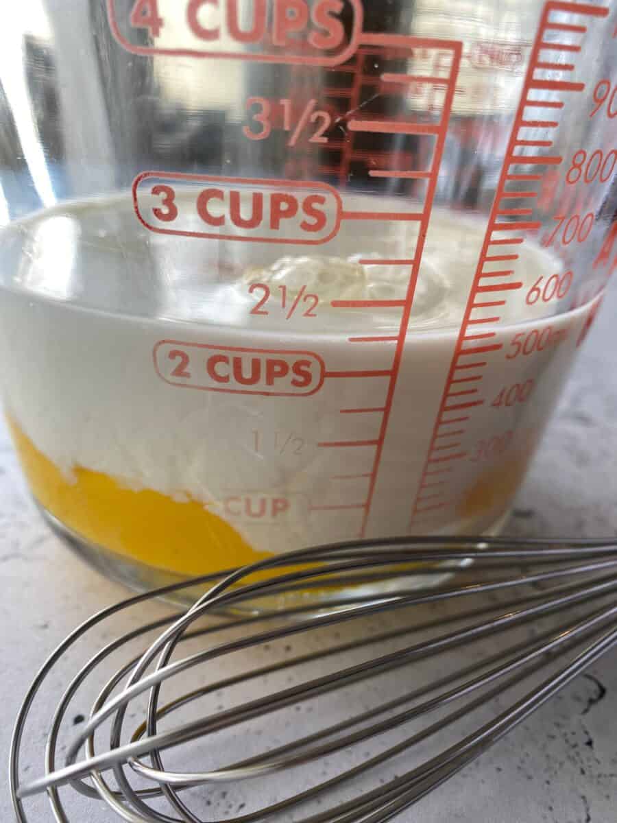 Milk and eggs in a measuring cup with a whisk on the side.