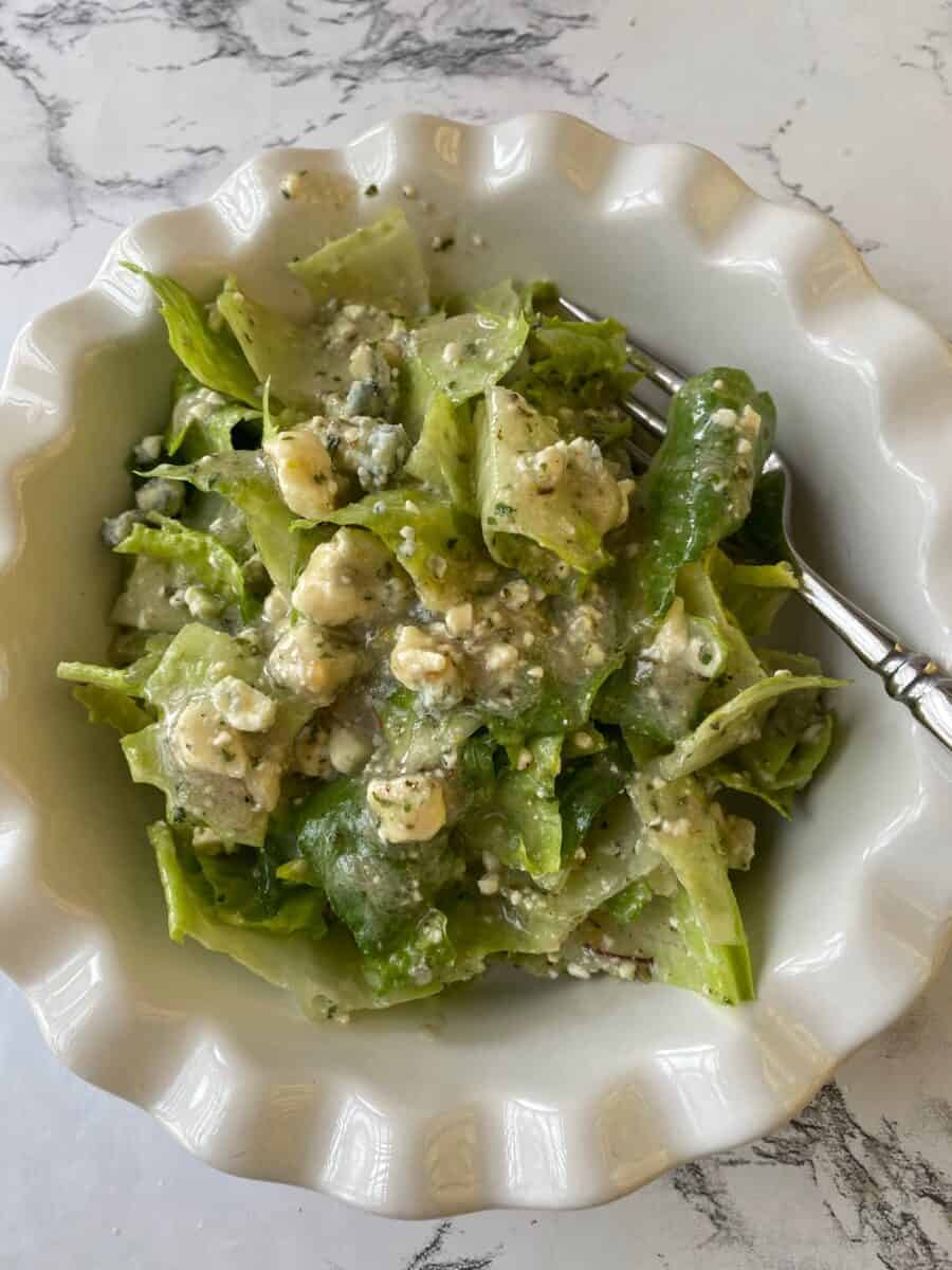 Salad greens in a small bowl covered with blue cheese vinaigrette, a copycat version of Buddy's Salad Dressing. 