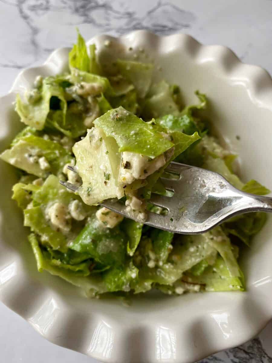 A fork full of green salad held above a bowl of salad.