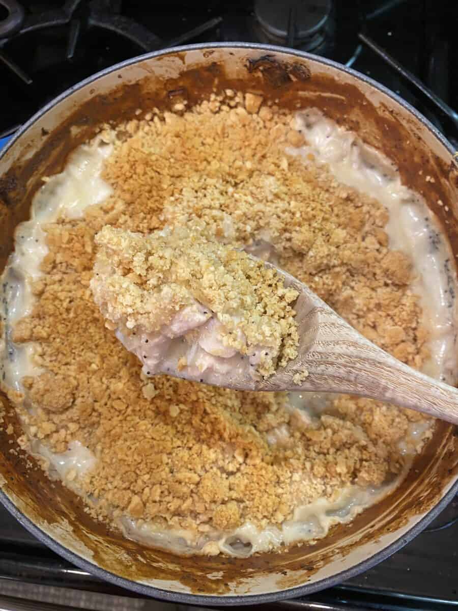 Cooked chicken casserole in a pot on the stove with a wooden spoon scooping up a serving.