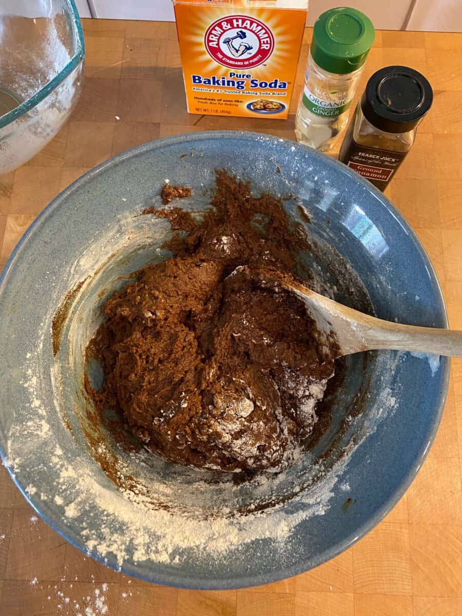 Mixing bowl with dough for snaps and a wooden spoon, with container of spices in the background.