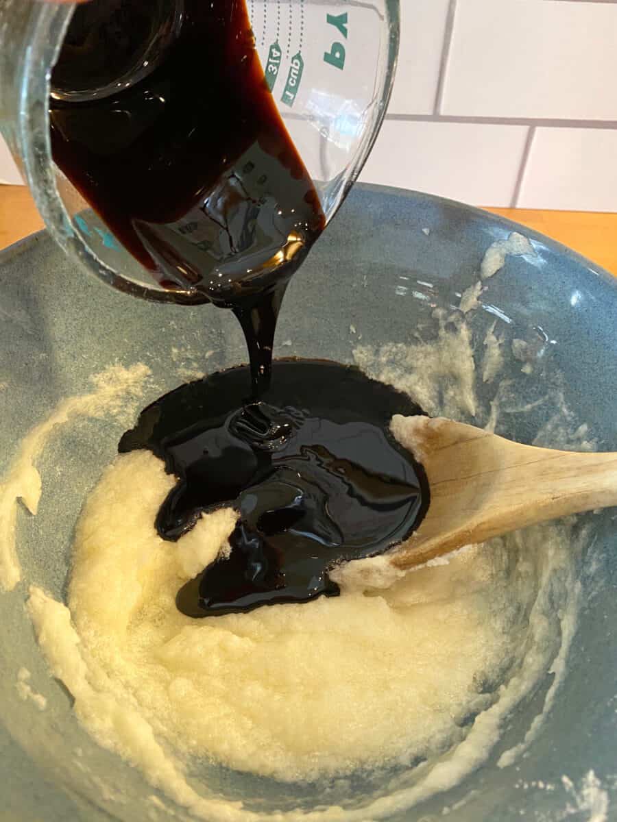 Molasses pouring into creamed ingredients in a bowl.