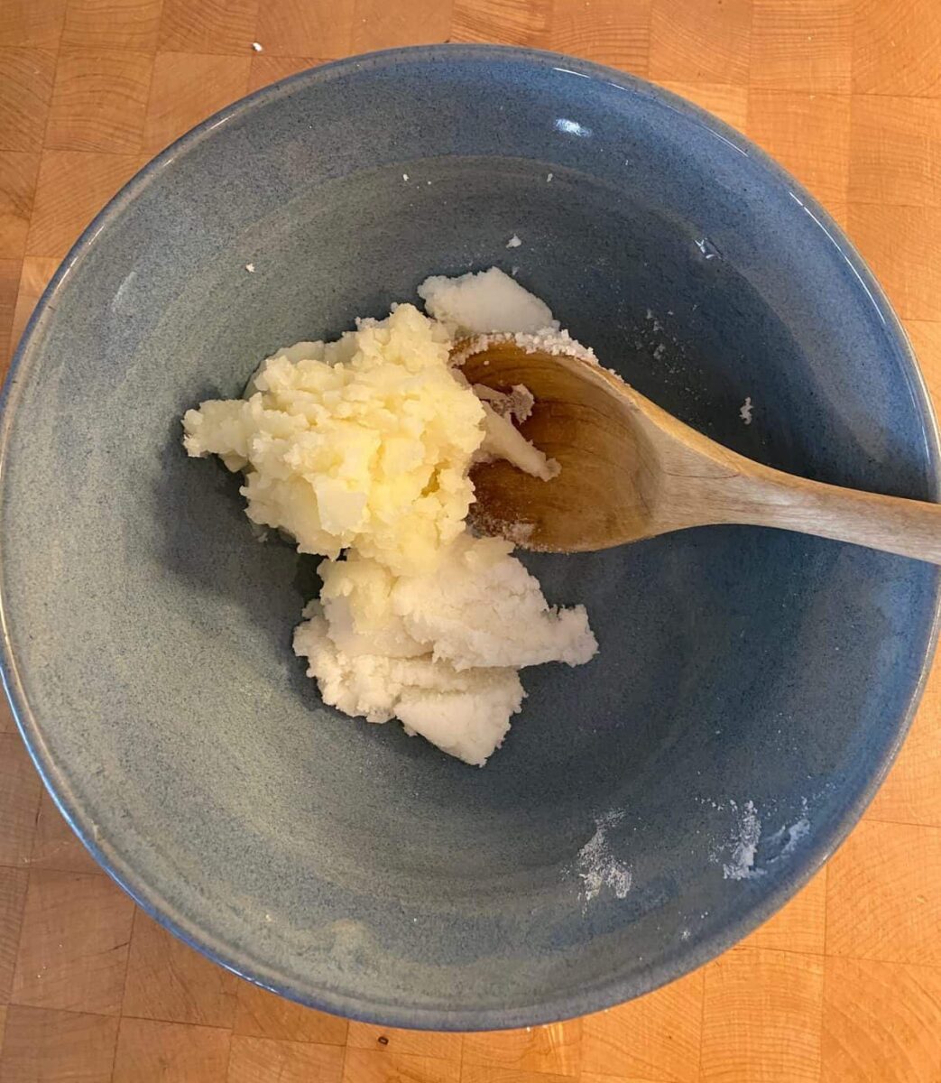 Mashed potatoes, shortening and sugar in a bowl with a wooden spoon.