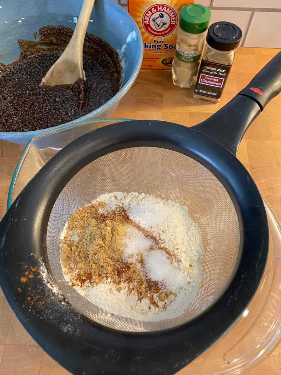 Dry ingredients in a whisk over a bowl, with containers of spices and another bowl off to the side.