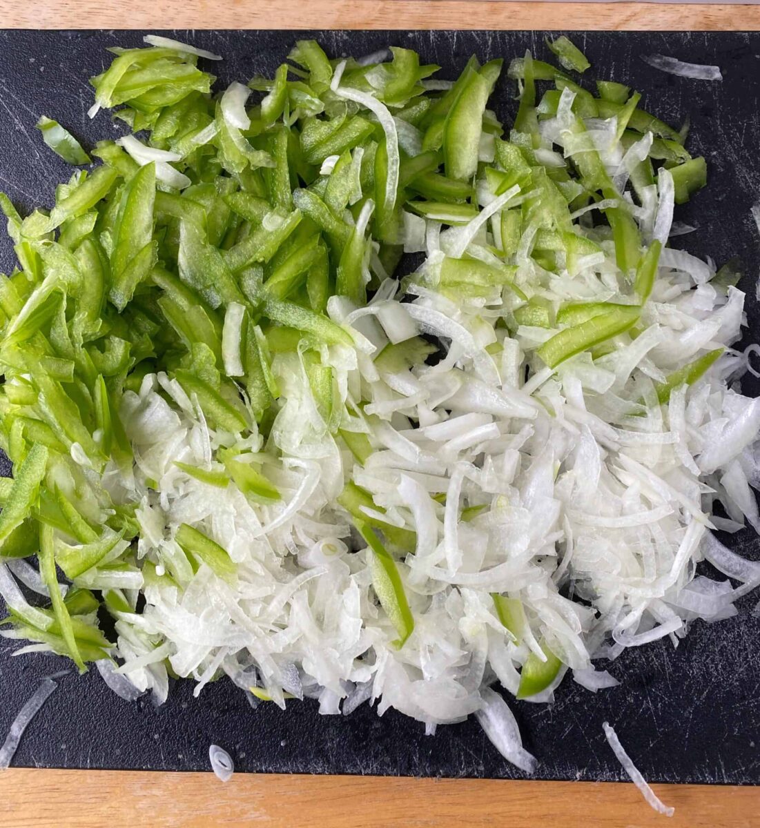 Sliced green pepper and onion on a cutting board.