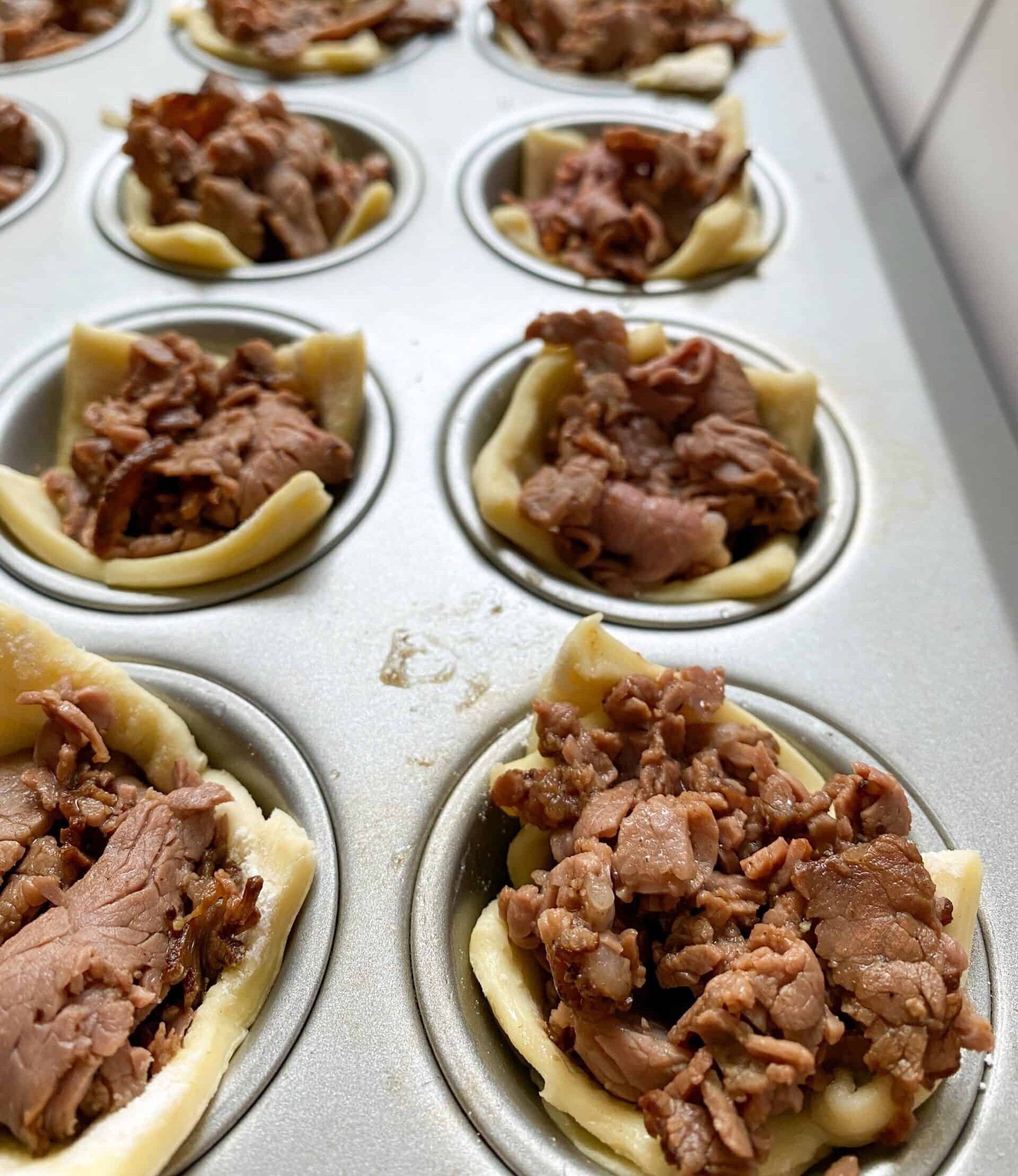 Mini muffin cups with cooked roast beef and puffed pastry in each one.