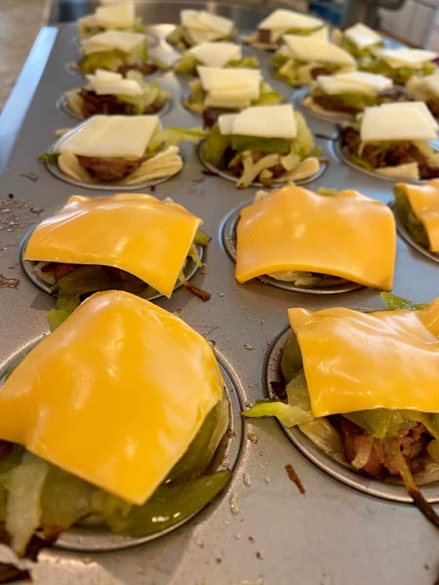 Mini Philly Cheesesteaks in a mini-muffin pan with melted cheese on top of each one.