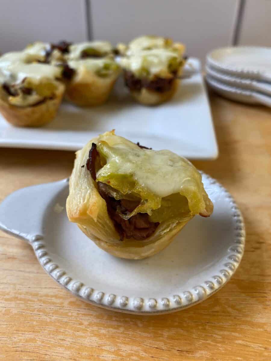 A Philly Cheesesteak Bite on a small plate, with a larger plate in the background and additional bites on display.