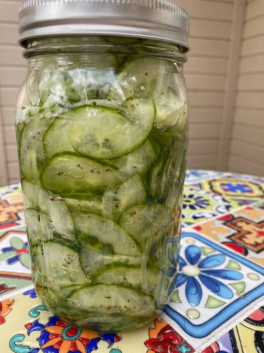 Sliced cucumbers and onions in a jar on a table.