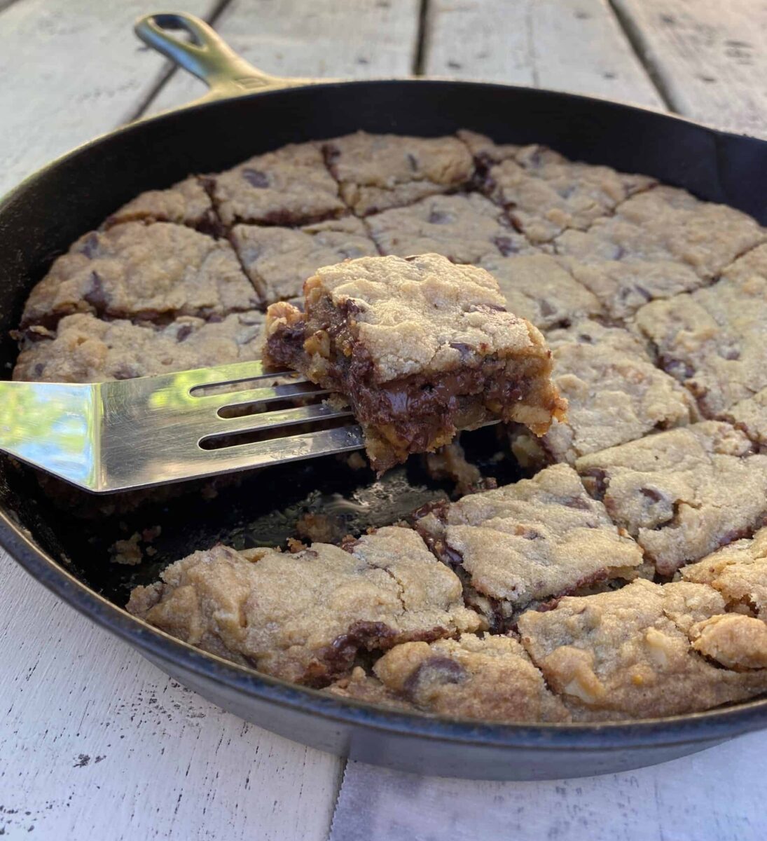 Chocolate chip bar cookie on a spatula, lifted out of a cast iron skillet.