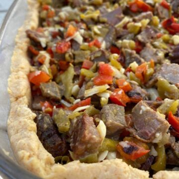 Diced beef with red peppers and green salsa in a tamale crust, all placed in a large glass dish.