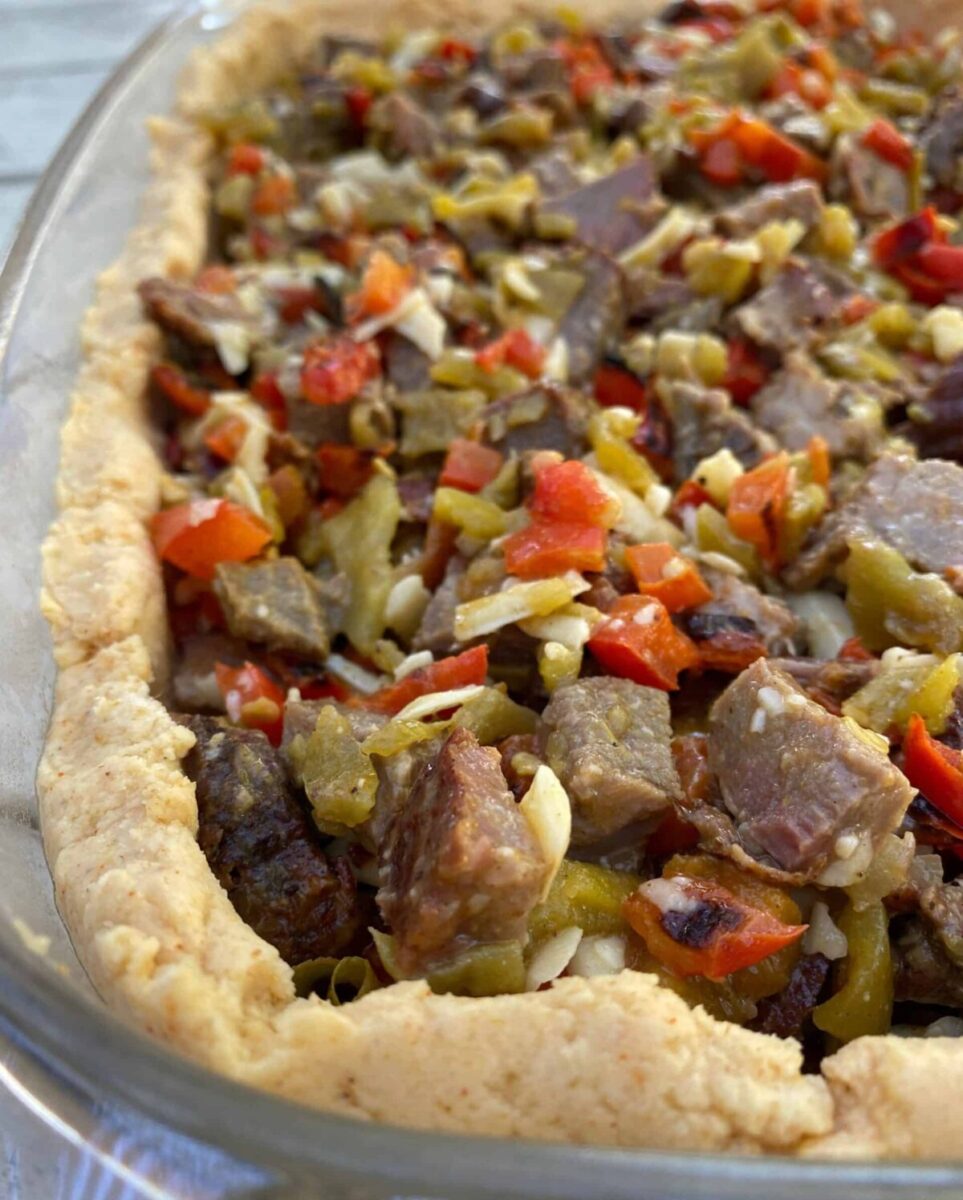 Diced beef with red peppers and green salsa in a tamale crust, all placed in a large glass dish.