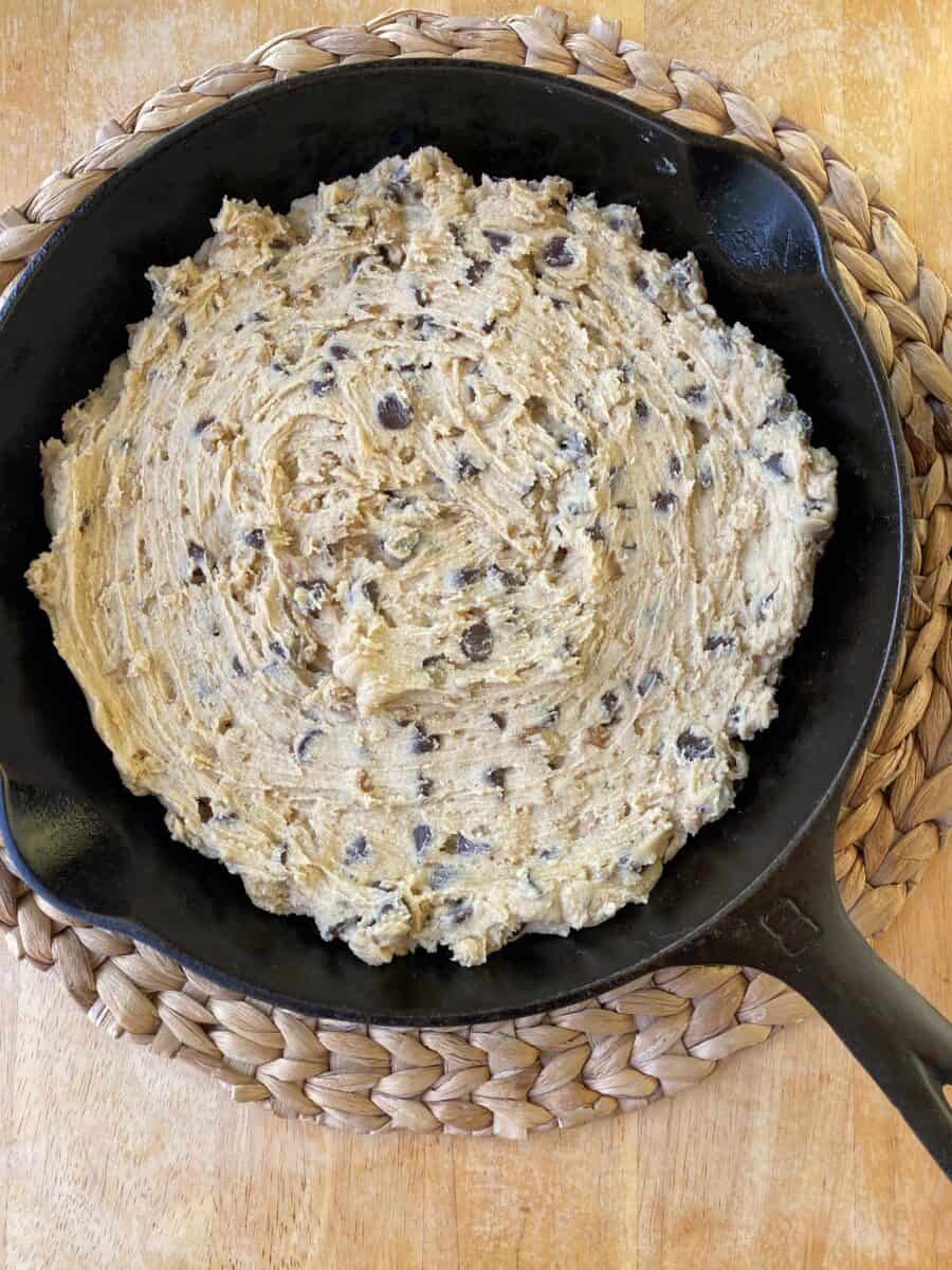 Unbaked bar cookie dough in a cast iron skillet on a cutting board.