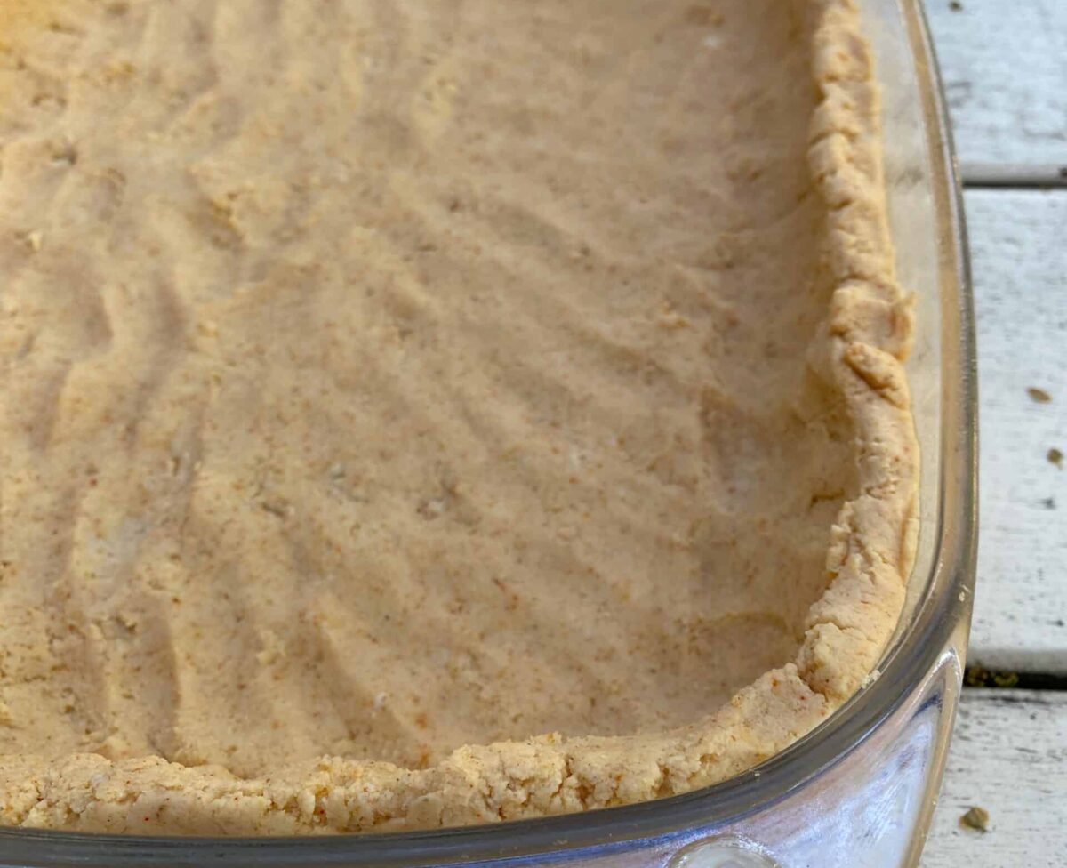 Tamale crust patted into a glass baking dish.