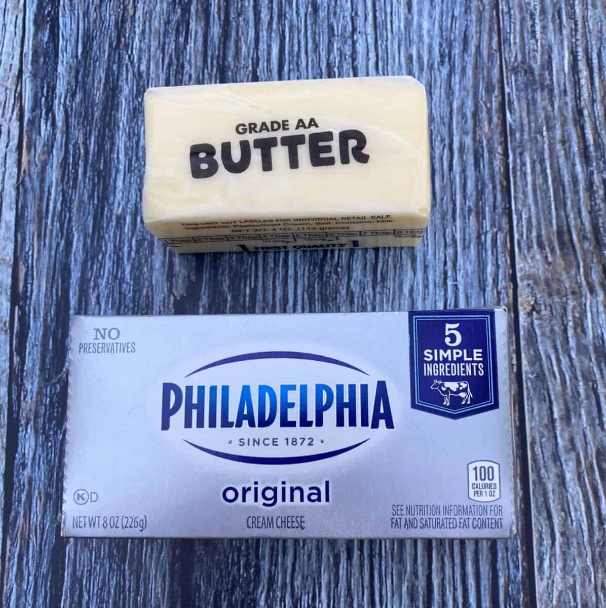 A stick of butter and a package of cream cheese on a wood block.