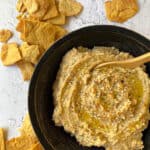 Cauliflower Hummus in a bowl with chips scattered on the table