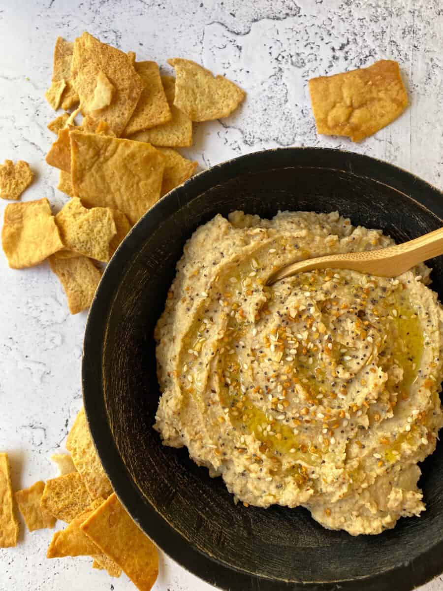 Cauliflower Hummus in a bowl with chips scattered on the table