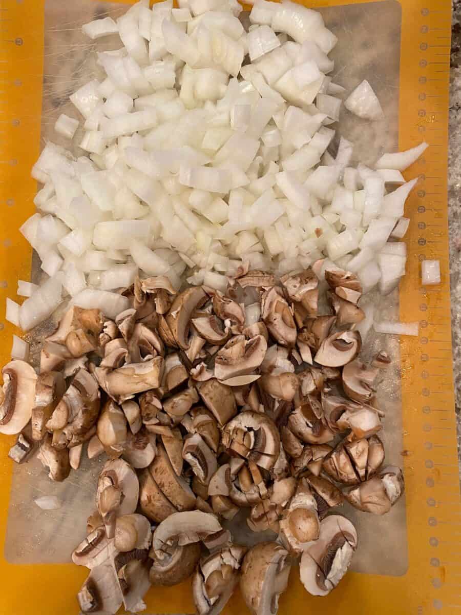 Diced mushrooms and onions on a cutting mat.