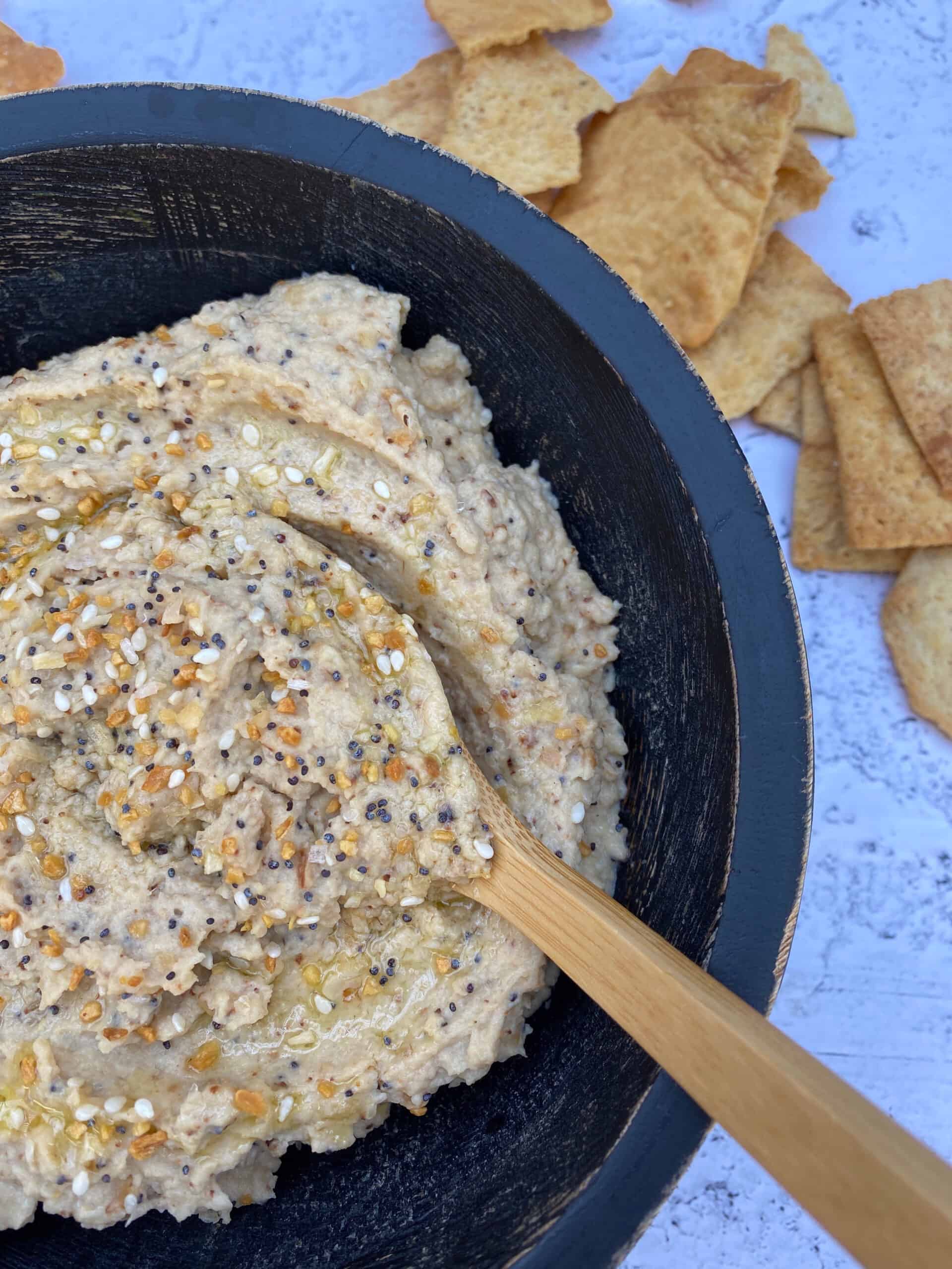 Hummus in a bowl with a small wooden spoon and pita chips on the side.