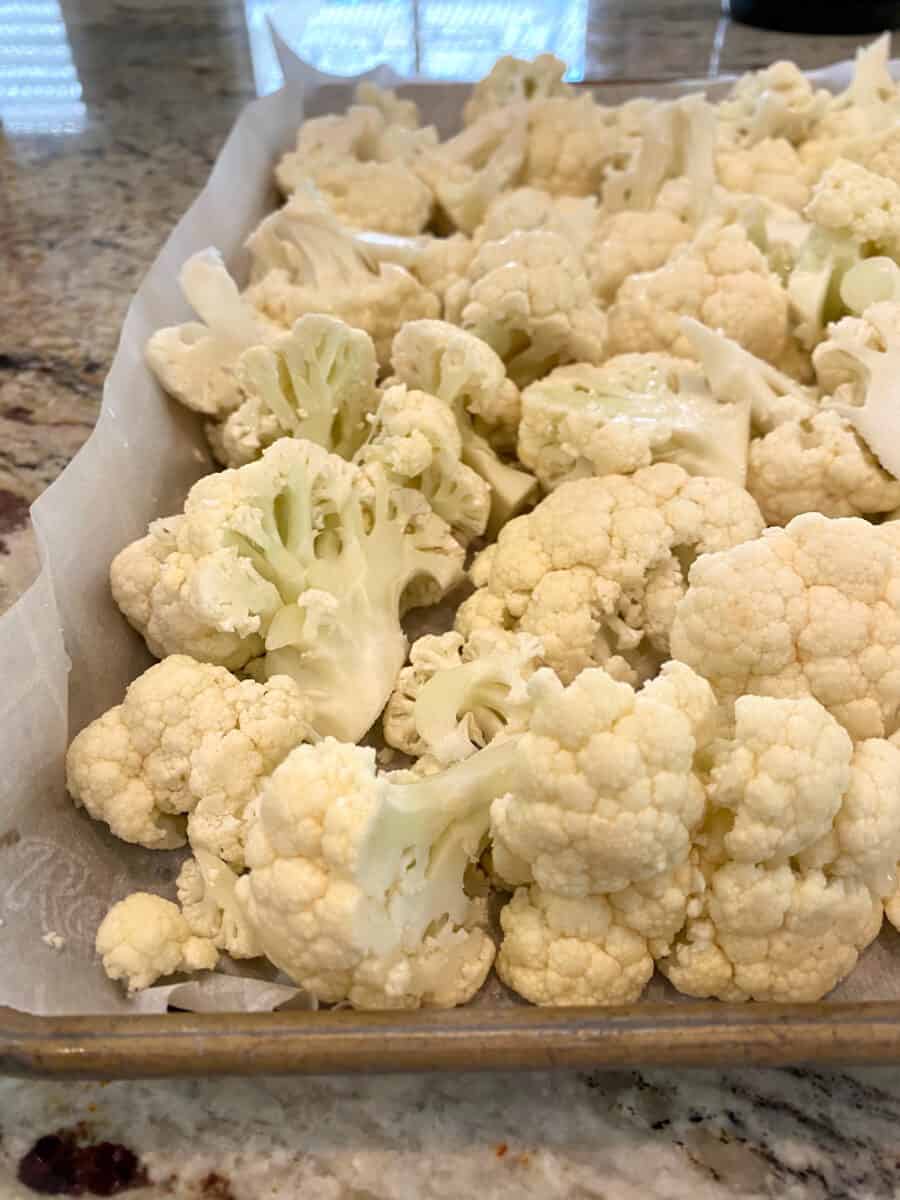 Raw cauliflower on a baking sheet lined with parchment paper. 