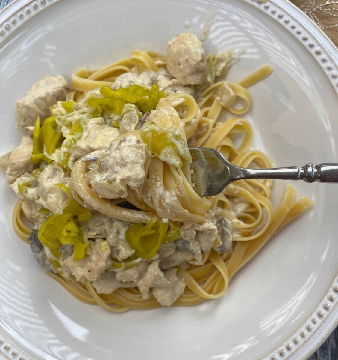 A serving of spicy chicken Alfredo on a plate with a fork that has a scoop of pasta and sauce.