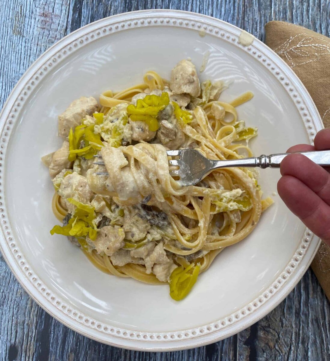 A serving of spicy chicken Alfredo on a plate with a fork and a napkin on the side.