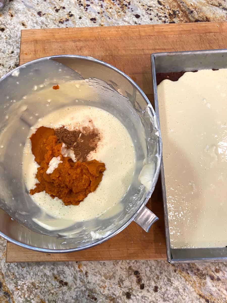 Pumpkin mixture and spices in a mixing bowl next to a pan of cream cheese batter.